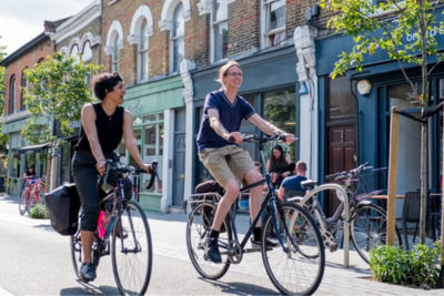 Two people cycling past some shops